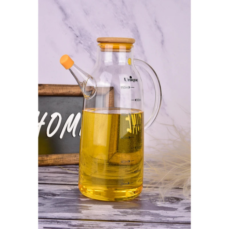 روغندان پیرکس یونیک روی میز چوبی حاوی روغن طلایی و درپوش نارنجی نازل